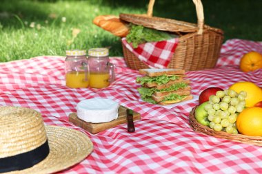 Dışarıdaki kareli battaniyenin üzerinde lezzetli yiyecek, içecek ve sofra takımı olan piknik sepeti.