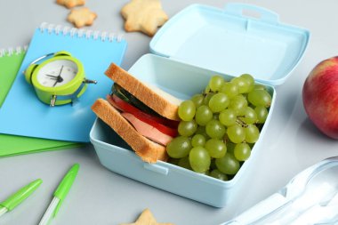 Beslenme çantası, bir şişe su, çalar saat ve beyaz masadaki kırtasiye malzemeleri.