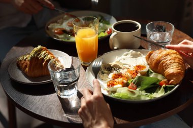 Kafedeki ahşap masada lezzetli bir kahvaltı yapan çift, yakın plan.