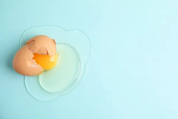 stock image Broken raw egg with shell on light blue background, top view. Space for text