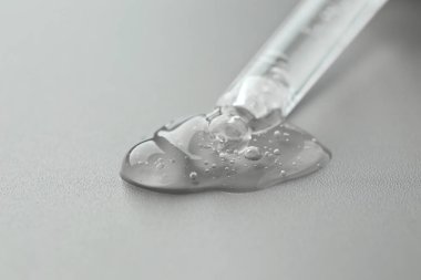 Gri arkaplandaki pipetten kozmetik serumu damlıyor, yakın plan.