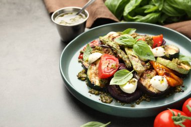 Izgara sebzeli lezzetli salata, pesto sosu ve gri desenli masada fesleğen, yakın plan. Metin için boşluk