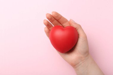 Woman holding red heart on pink background, top view. Space for text