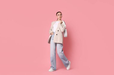 Pembe arka planda çantası olan bej ceketli şık bir kadın.