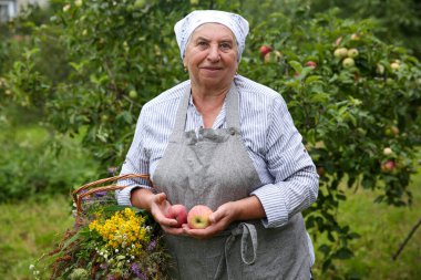 Dışarıda elma ve kır çiçekleriyle kıdemli bir kadın.