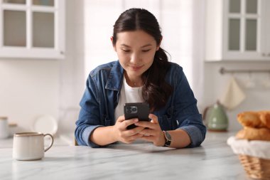 Mutfaktaki masada akıllı telefon kullanan güzel bir kadın.