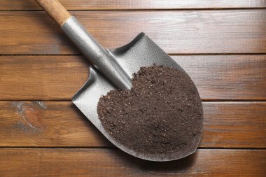 Tahta masanın üzerinde toprak olan metal kürek, üst manzara.