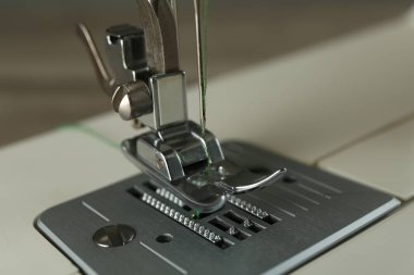Gri arkaplanda yeşil iplikli dikiş makinesi, yakın plan
