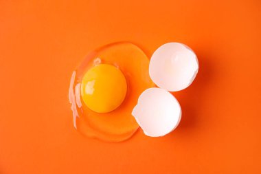 Turuncu arka planda kırılmış çiğ yumurta ve kabuk.