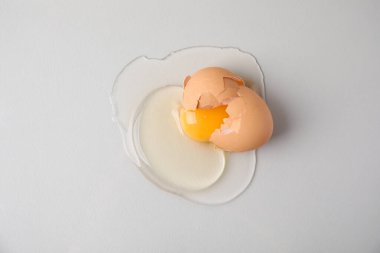 Broken raw egg with shell on light grey background, top view clipart