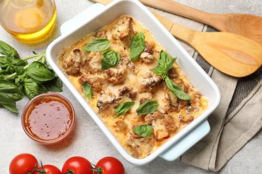 Fırında pişmiş karnabahar, fesleğen, sos, domates ve yağ açık gri masada, üst görünümde.