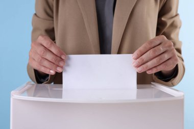 Kadın oyunu açık mavi arka plana karşı sandığa koyuyor, yakın plan.