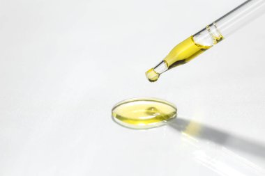 Açık gri arka planda pipetten süzülen kozmetik yağı, yakın plan