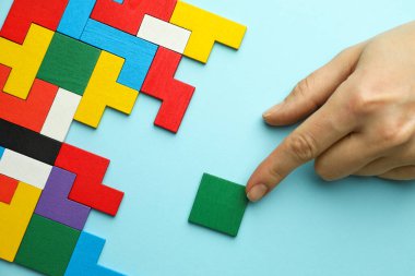 Açık mavi arka planda renkli ahşap yapboz parçalarıyla oynayan kadın, üst görünüm