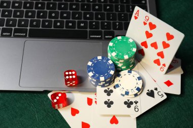 Poker chips, laptop, playing cards and dices on green table. Online game