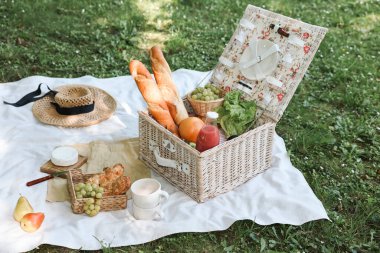 Açık havada piknik sepeti, lezzetli yiyecekler, sofra takımı ve içecek.