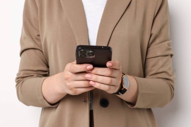 Beyaz arka planda akıllı telefon kullanan bej elbiseli kadın, yakın plan.