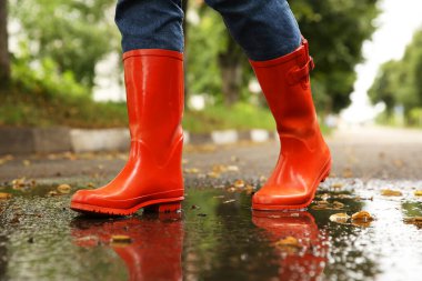 Turuncu lastik çizme giyen bir kadın açık havada su birikintisinde yürüyor.