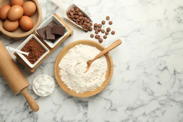 stock image Flat lay composition with flour, chocolate and other ingredients for making dough on white marble table. Space for text