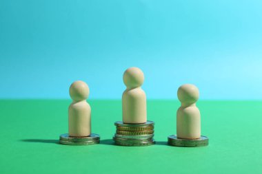 Finansal eşitsizlik. Yeşil arka planda farklı yükseklikteki istiflenmiş paraların tahta figürleri