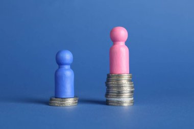 Finansal eşitsizlik. Erkek ve kadın figürleri mavi arkaplana karşı farklı yükseklikte istiflenmiş paralar üzerinde