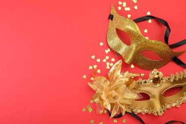 Kırmızı arka planda altın karnaval maskeleri ve konfeti, üst manzara. Metin için boşluk