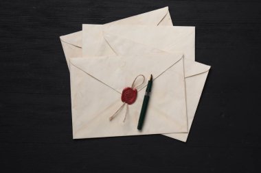 Eski mektup zarfları ve dolma kalemle siyah ahşap masa, üst manzara.