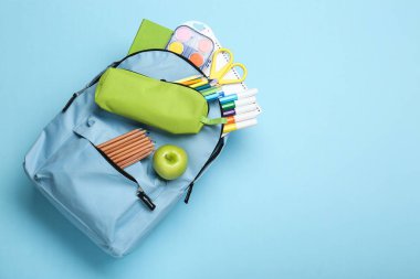 Açık mavi arka planda farklı okul kırtasiyesi olan sırt çantası, üst görünüm. Metin için boşluk