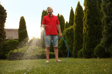 Bahçede hortumla çimenleri sulayan bir adam.