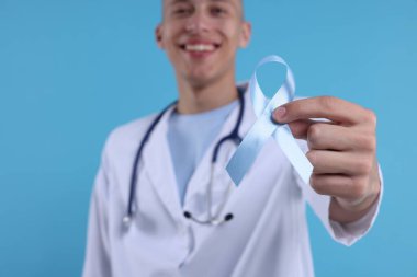 Prostat kanseri farkındalığı. Doktor, açık mavi kurdeleyi renk arkaplanı ve seçici odak üzerine desteğin sembolü olarak tutuyor