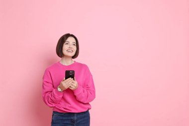 Pembe arka planda akıllı telefonu olan gülümseyen bir kadın. Metin için boşluk