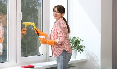 Cam sileceği ve sprey deterjan şişesi olan güzel genç bir kadın.