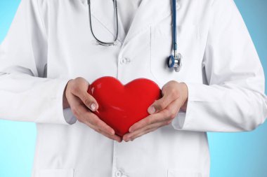Açık mavi arka planda kırmızı kalpli doktor, yakın plan.
