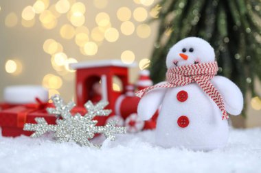 Kardan adam figürü ve bulanık ışıklara karşı yapay kar üzerindeki diğer Noel dekorları.