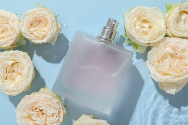 Güzel gül çiçekleri ve parfüm şişesi açık mavi arka planda suda, düz yatıyordu.