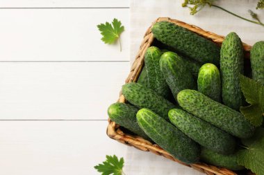 Hasır kutuda taze yeşil salatalıklar ve beyaz ahşap masada baharatlar, üst manzara. Metin için boşluk