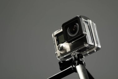 Gri arka planda modern aksiyon kamerası ve tripod, yakın plan. Metin için boşluk
