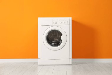 Bir çamaşır makinesi turuncu duvarın yanında.