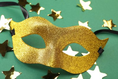 Yeşil arka planda bir altın karnaval maskesi ve konfeti, yakın plan.