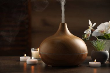 Aroma yağı yayıcı, yanan mumlar ve ahşap masa üzerinde bitkiler.
