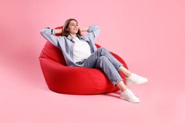 Gülümseyen kadın pembe arka planda kırmızı fasulye koltukta oturuyor.