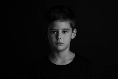 Karanlık arka planda üzgün küçük bir çocuğun portresi. Siyah ve beyaz etkisi