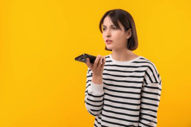 Sarı arkaplanda akıllı telefondan sesli mesaj kaydeden güzel bir kadın, metin için boşluk