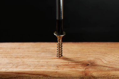 Vidaları tahta tahtaya vidalamak karanlık arka plana karşı, yakın plan