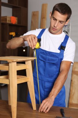 İçerideki ahşap tabureyi tamir ederken mezura kullanan bir adam.