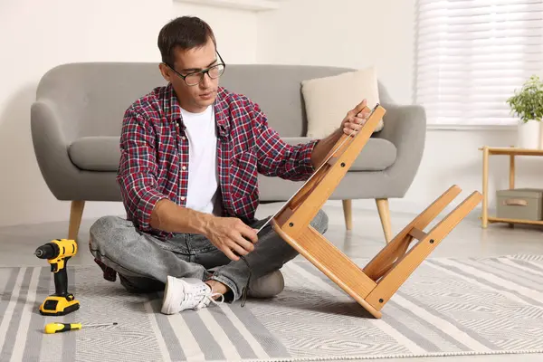 stock image Man using tape measure while repairing wooden stool indoors