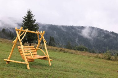 Tahta salıncak ve sabah sisle kaplı dağlar.