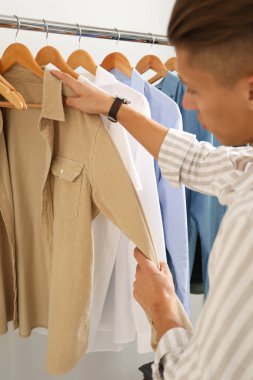 Gömlekli bir adam iç mekânda elbise seçiyor.