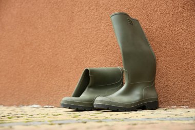 Duvarın yakınındaki kaldırımda gri lastik çizmeler.