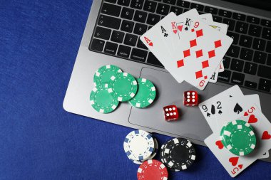 Poker fişleri, dizüstü bilgisayar, kağıt ve zarlar mavi masada, düz konum. Çevrimiçi oyun